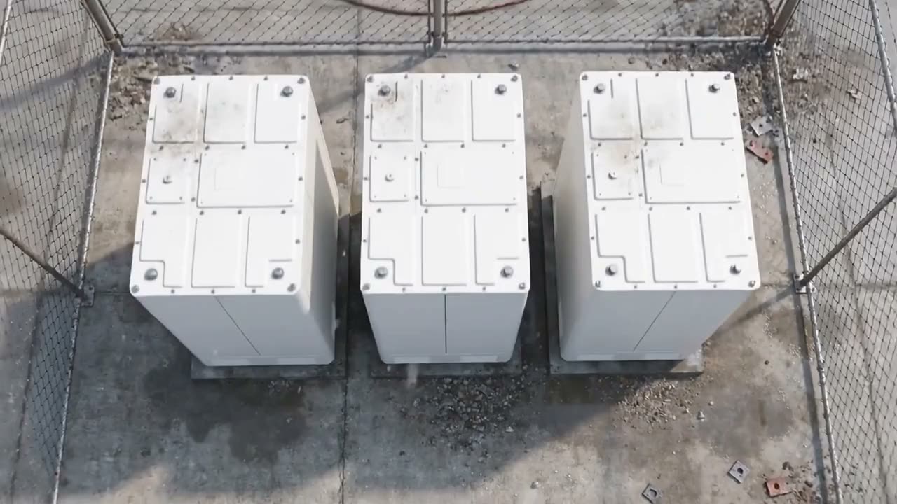 Three white battery containers inside a chain-link fence